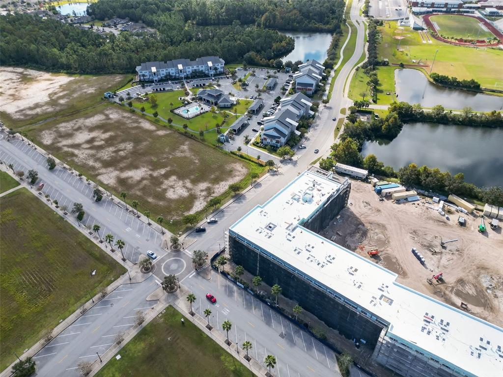 An aerial view shows a large, multi-story apartment building under construction near a lake — 890 CENTRAL AVENUE UNIT A107B, PALM COAST, FL