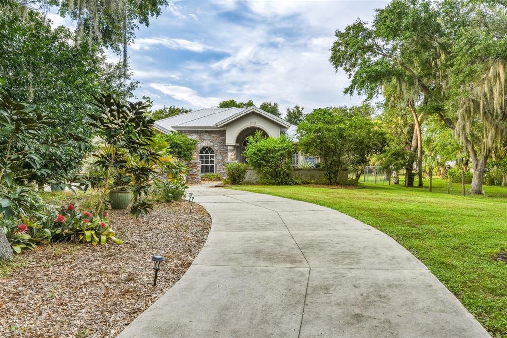 A single-story house with a stone facade, metal roof, and a concrete driveway — 8596 SW RIVERSIDE DRIVE, ARCADIA, FL