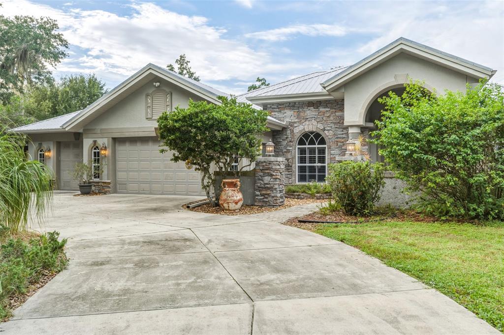 A stone-paved walkway leads to the arched entryway of a house with stone veneer accents — 8596 SW RIVERSIDE DRIVE, ARCADIA, FL