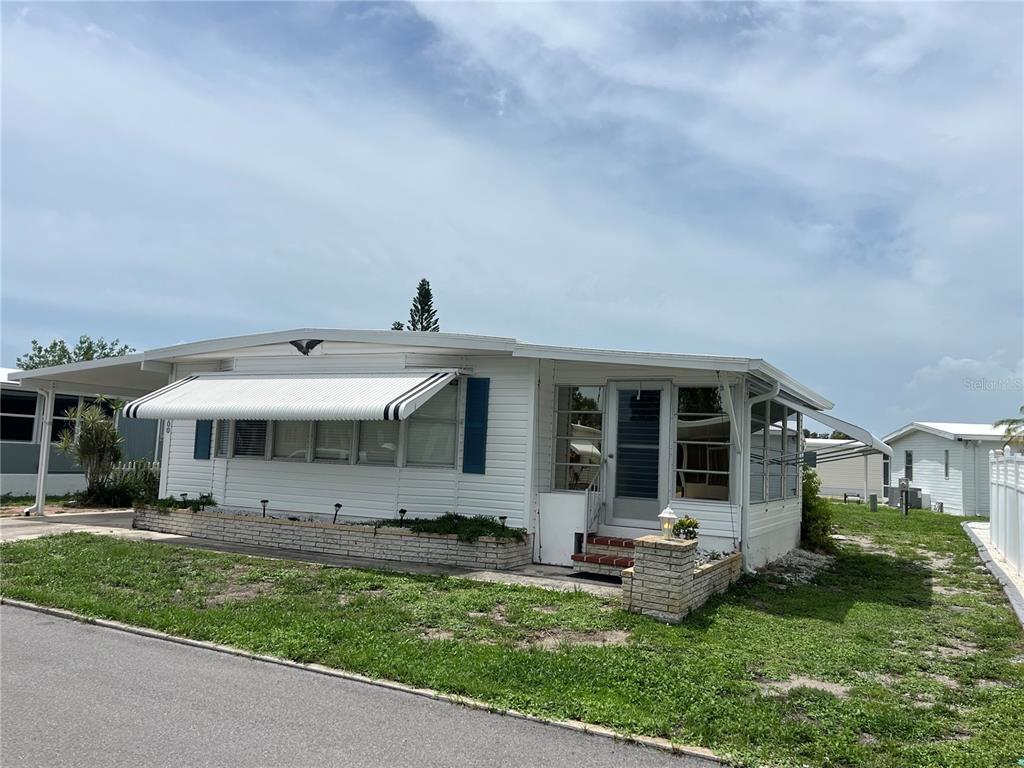 A white mobile home with a metal awning and a small brick planter box exterior — 900 JOLANDA CIRCLE, VENICE, FL