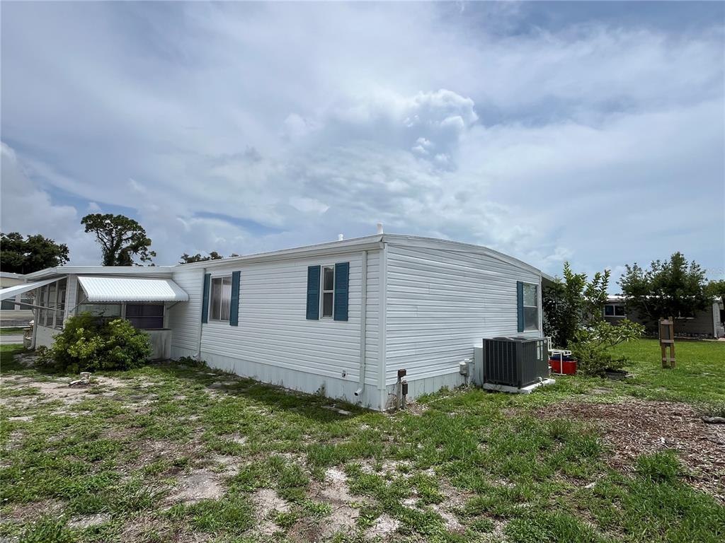 A white mobile home with blue shutters sits on a grassy lot under a cloudy sky — 900 JOLANDA CIRCLE, VENICE, FL
