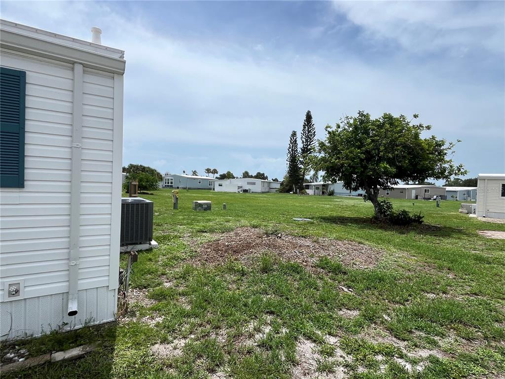 A view of a grassy yard with a tree and neighboring mobile homes — 900 JOLANDA CIRCLE, VENICE, FL