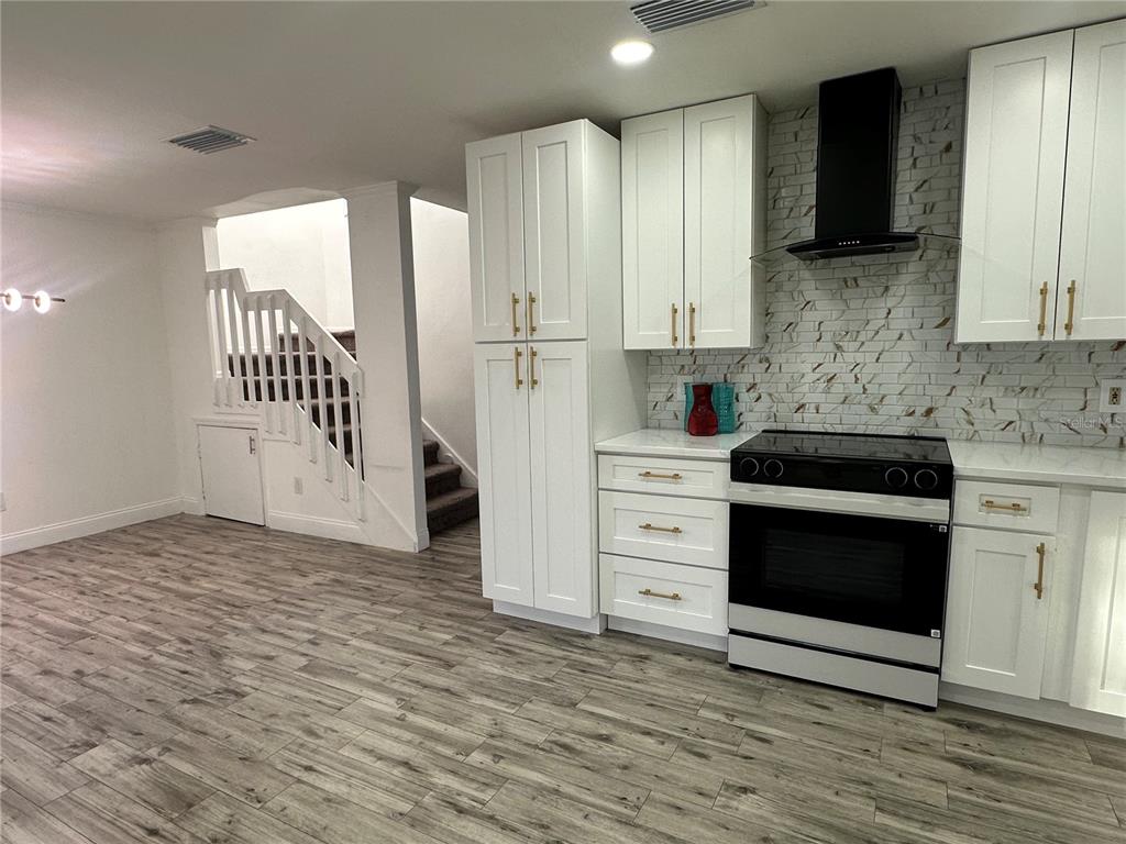 A kitchen features white cabinets, a black range, and a marble-style backsplash near a staircase — 9224 VENTANA LANE, ORLANDO, FL