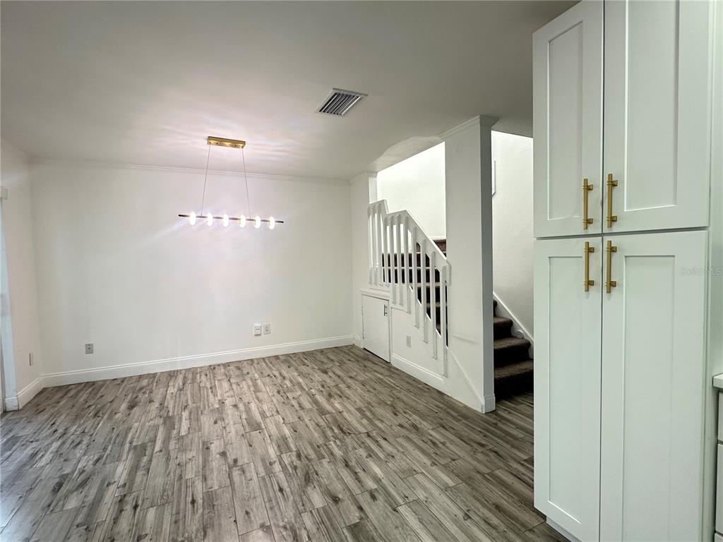 A dining area features light wood-look flooring, a modern linear chandelier, and a white staircase — 9224 VENTANA LANE, ORLANDO, FL