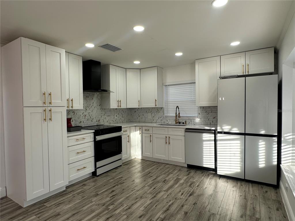 A modern kitchen features white shaker cabinets, stainless steel appliances, and wood-look flooring — 9224 VENTANA LANE, ORLANDO, FL