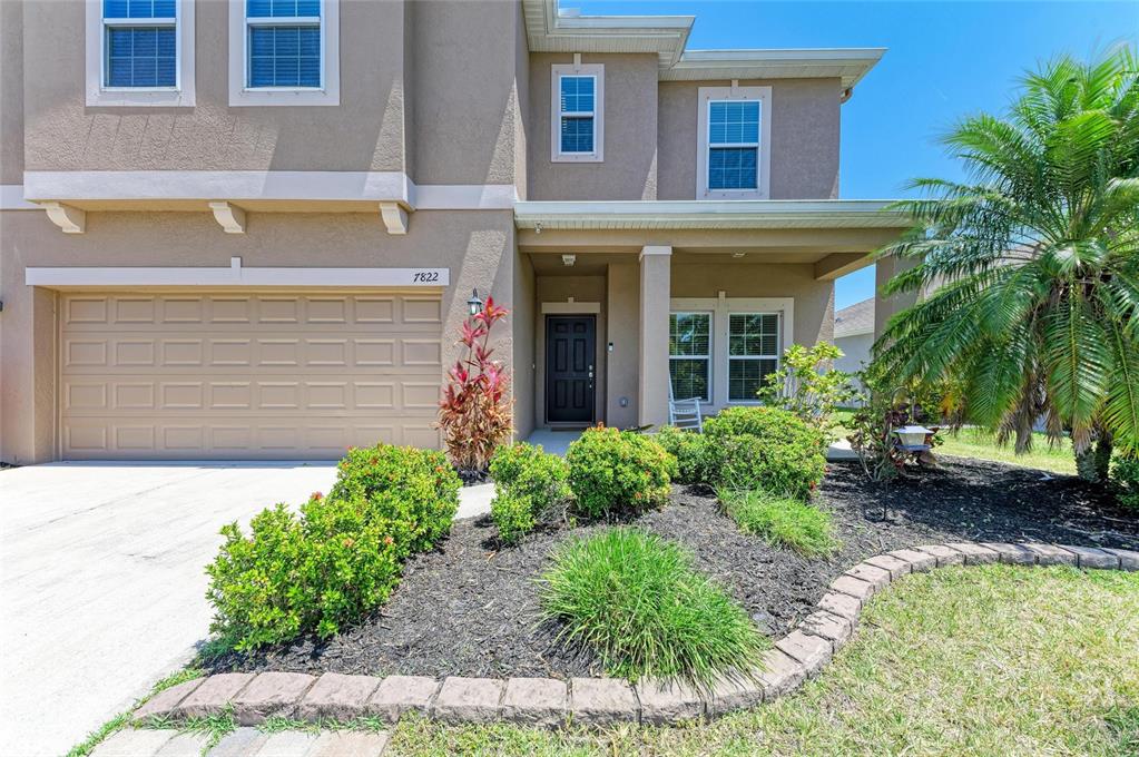 A two-story tan stucco house features a two-car garage, front porch, and landscaped yard — 7822 110TH AVENUE E, PARRISH, FL