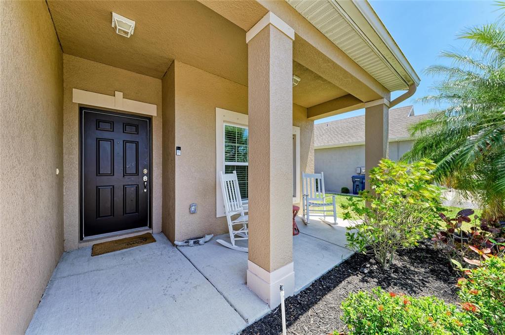 A covered front porch features a dark door, two white rocking chairs, and concrete flooring — 7822 110TH AVENUE E, PARRISH, FL