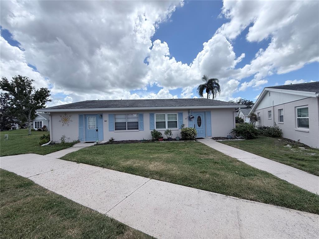 A single-story duplex with light-colored siding, blue shutters, and two front doors — 402 DORCHESTER PLACE UNIT 44, SUN CITY CENTER, FL