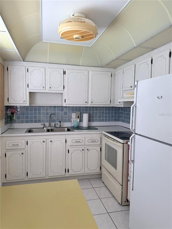 A kitchen features white wood-grain cabinets, blue tiled backsplashes, a yellow countertop, and a ceiling fan — 402 DORCHESTER PLACE UNIT 44, SUN CITY CENTER, FL