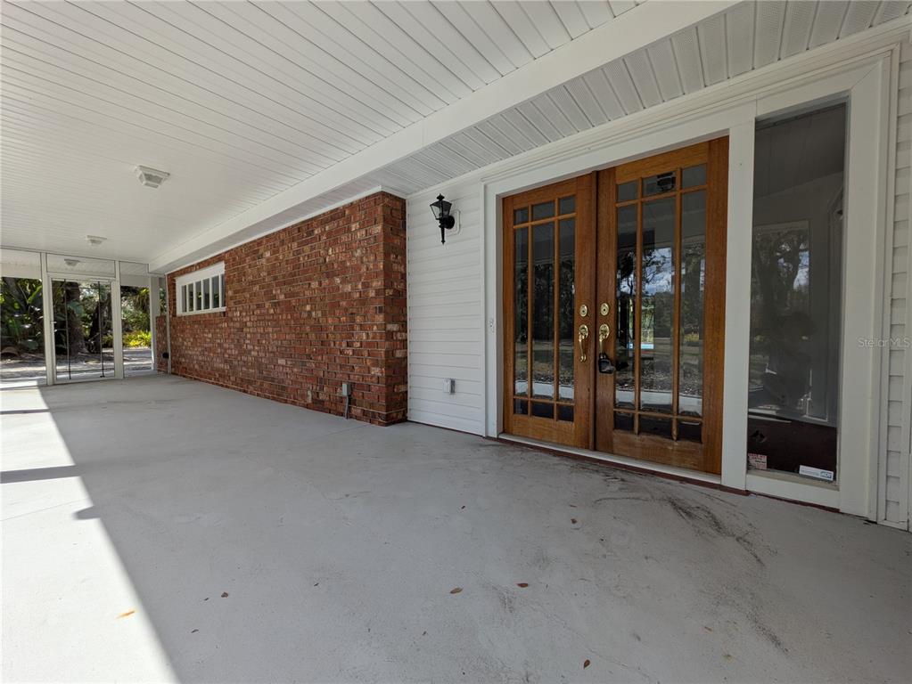 A covered patio features a brick wall, white siding, and double wooden glass doors — 4554 COOPER ROAD, SARASOTA, FL
