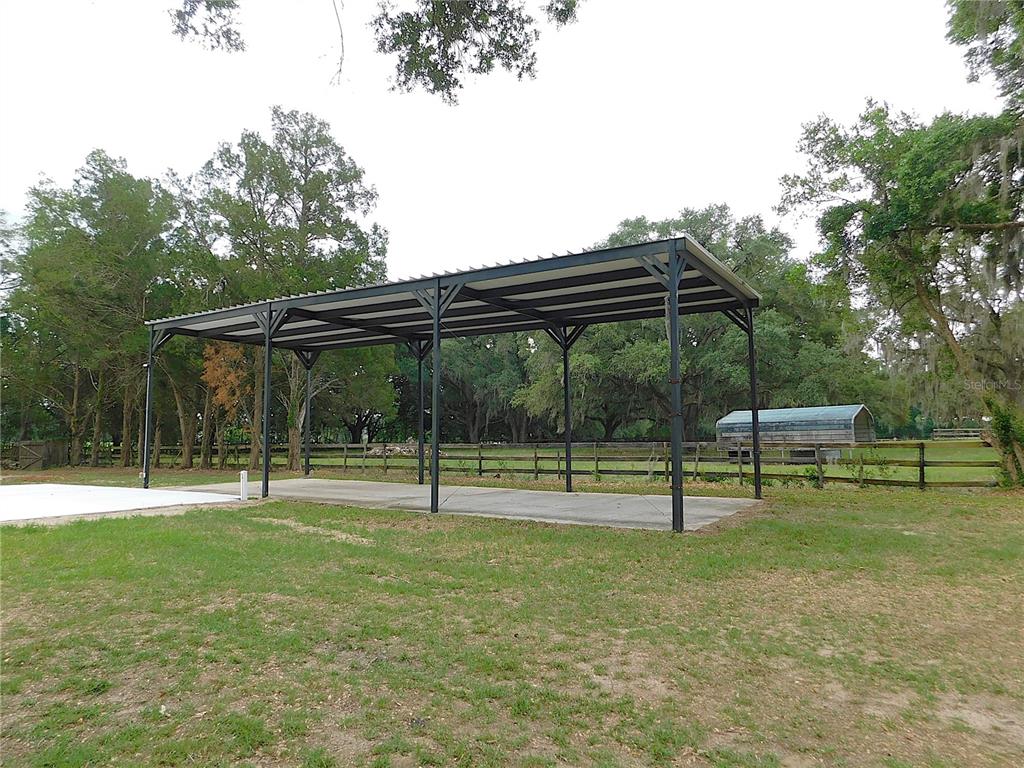 A metal carport stands on a concrete slab in a grassy, tree-lined yard — 6875 NE 25TH AVENUE, OCALA, FL