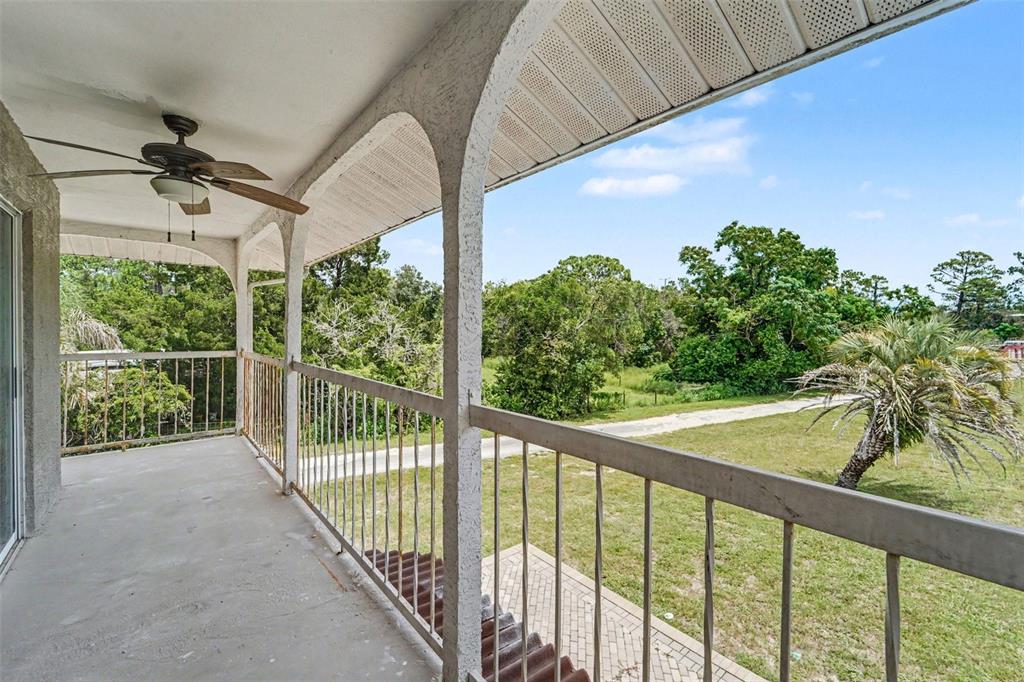 A covered balcony with a ceiling fan, metal railing, and views of trees and grass — 6446 LUCKY LANE, SPRING HILL, FL