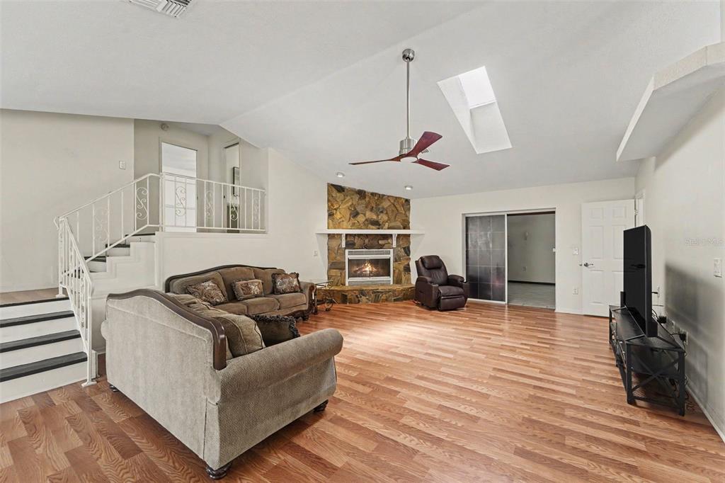 A living room with wood flooring, a stone fireplace, a ceiling fan, and a staircase — 6446 LUCKY LANE, SPRING HILL, FL