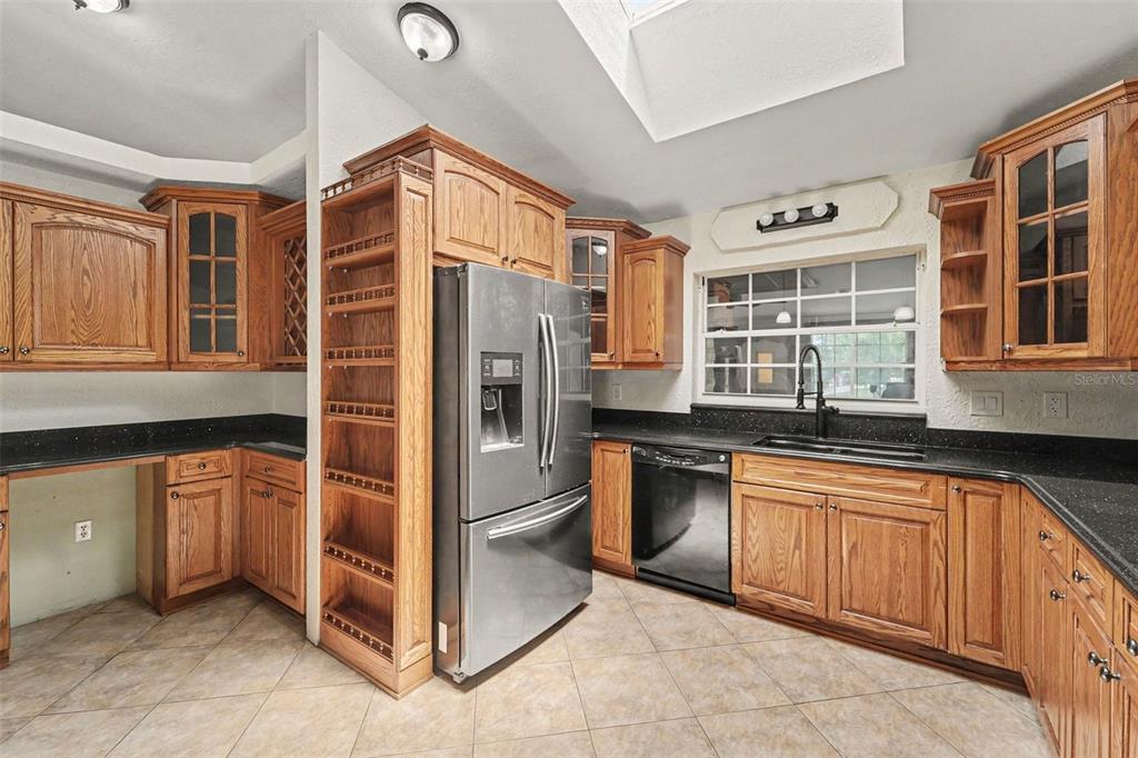 A kitchen with wood cabinets, black countertops, stainless steel appliances, and tile flooring — 6446 LUCKY LANE, SPRING HILL, FL