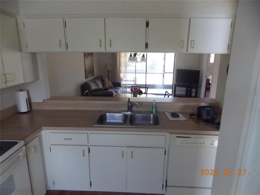 A kitchen features white cabinets, a double-basin sink, and a pass-through window to the living area — 26267 NORTHERN CROSS ROAD UNIT 6C, PUNTA GORDA, FL