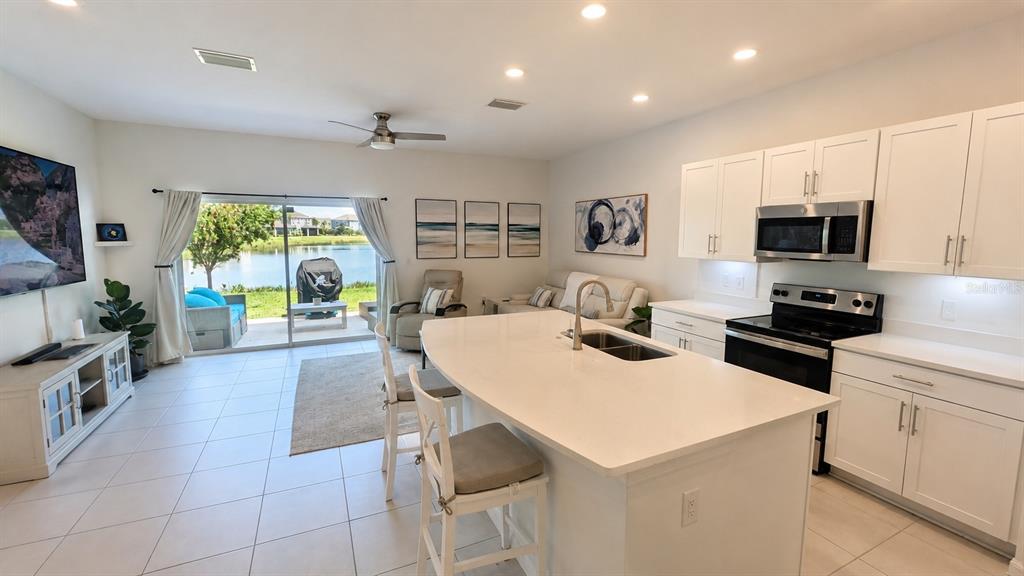 An open-concept kitchen and living area features a white island, stainless appliances, and sliding glass doors — 5698 ARCHIPELAGO STREET, NOKOMIS, FL