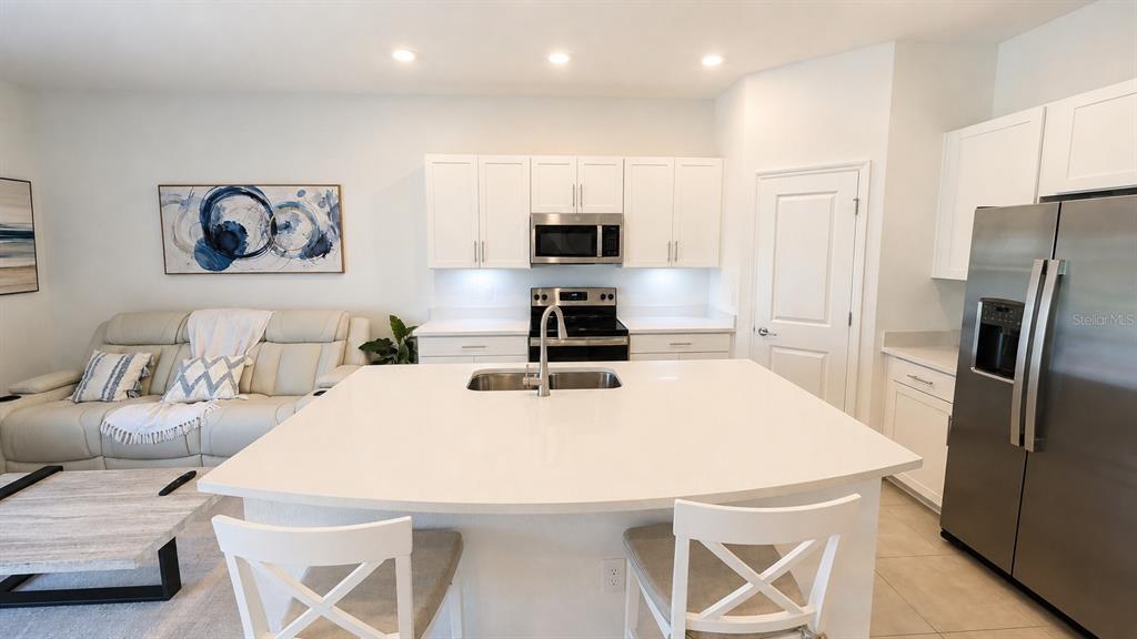 A kitchen with white cabinets, stainless steel appliances, and a large island faces a living area — 5698 ARCHIPELAGO STREET, NOKOMIS, FL