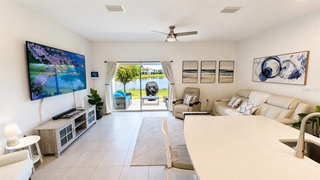 A living room features a large television, a beige sofa, and sliding doors overlooking a lake — 5698 ARCHIPELAGO STREET, NOKOMIS, FL