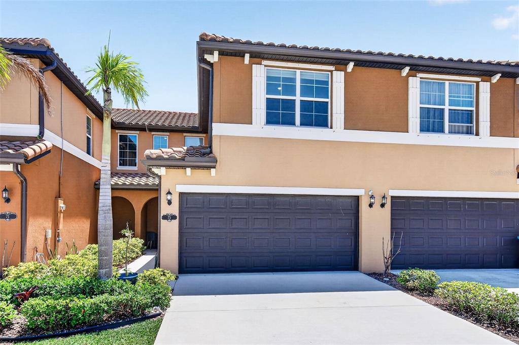 The exterior of a two-story tan townhouse features a dark brown two-car garage — 73 MONTECITO DRIVE, SATELLITE BEACH, FL