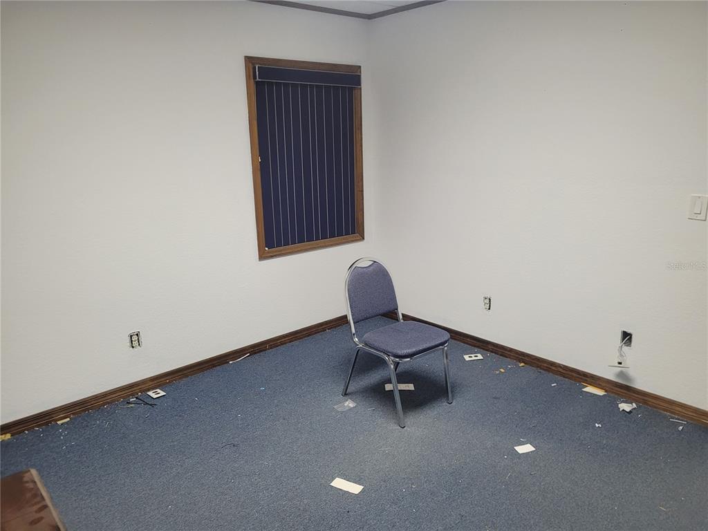 An empty office room features white walls, blue carpeting, a single chair, and a window — 8875 E HIGHWAY 25, BELLEVIEW, FL