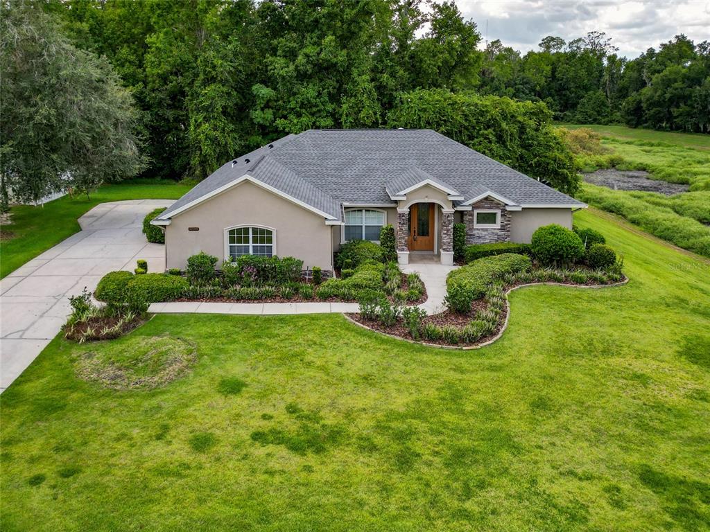 An aerial view of a single-story house with a tan exterior, gray roof, and landscaping — 10040 SE 42ND COURT, BELLEVIEW, FL
