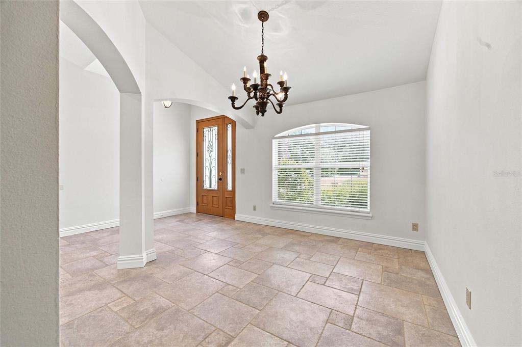 A bright dining room features tile flooring, an arched entryway, and a traditional chandelier — 10040 SE 42ND COURT, BELLEVIEW, FL