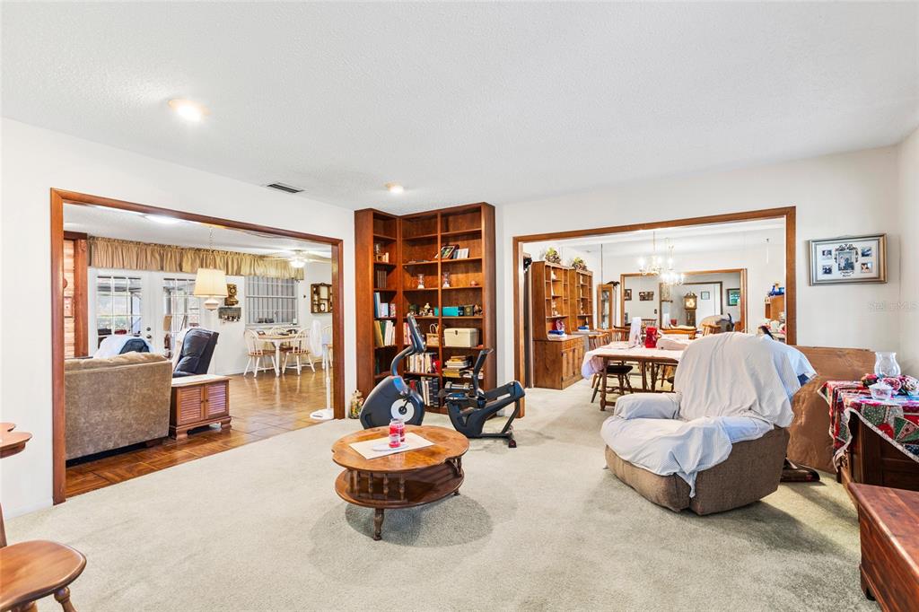 A carpeted living room features a wooden bookshelf, exercise equipment, and views into adjacent rooms — 7797 132ND WAY, SEMINOLE, FL