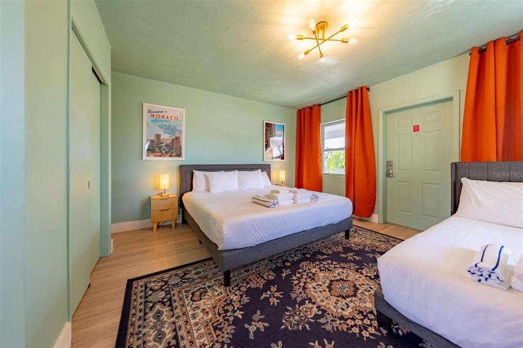 A bedroom features two beds, a patterned rug, and orange curtains against light green walls — 333 HAMDEN DRIVE, CLEARWATER BEACH, FL