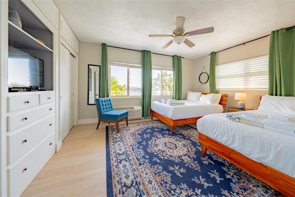 A bedroom features two beds, a blue armchair, a large patterned rug, and green curtains — 333 HAMDEN DRIVE, CLEARWATER BEACH, FL