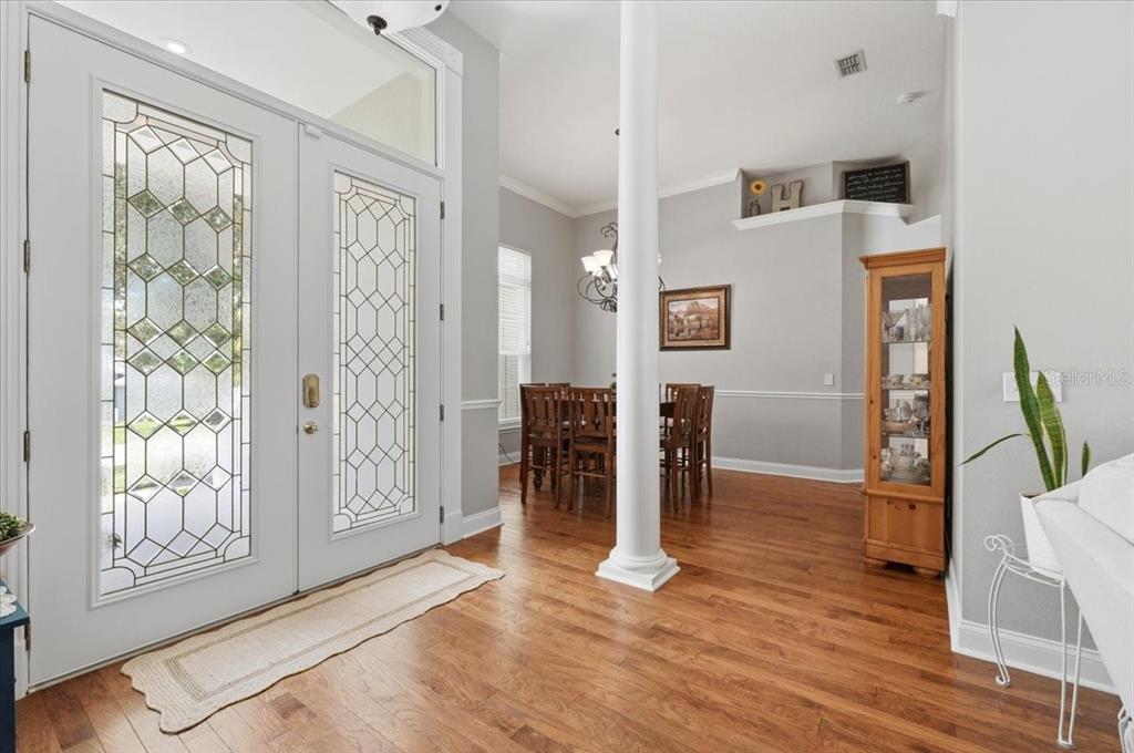 A bright entryway with hardwood floors, a white column, and a view into the dining room — 5618 SUMMERLAND HILLS DRIVE, LAKELAND, FL