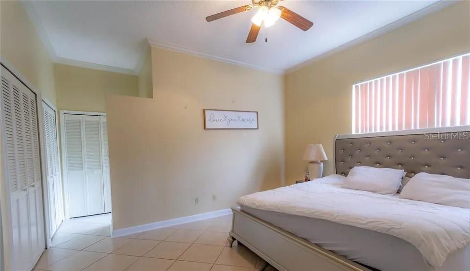A bedroom features a tufted headboard, tile flooring, a ceiling fan, and white louvered closet doors — 2545 CLARINET DRIVE, ORLANDO, FL