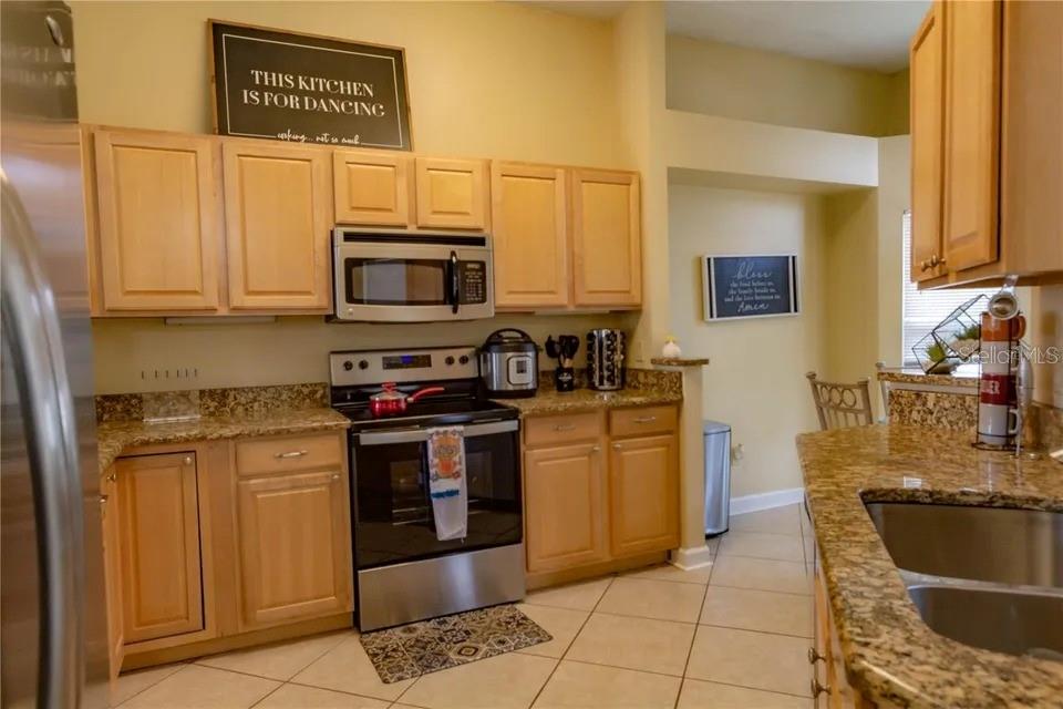 A kitchen features light wood cabinets, granite countertops, stainless steel appliances, and tile flooring — 2545 CLARINET DRIVE, ORLANDO, FL