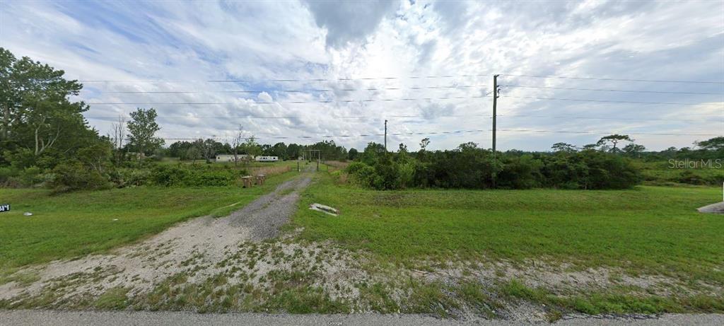 A gravel driveway leads from a paved road toward a distant mobile home on grassy land — 11300 E IRLO BRONSON MEMORIAL HIGHWAY, ST CLOUD, FL
