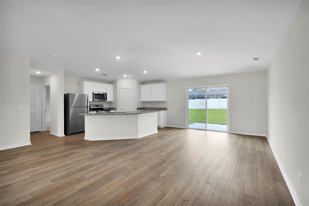 An open-concept kitchen and living area featuring light wood flooring, white cabinets, and sliding doors — 2 RYMSHAW PLACE, PALM COAST, FL