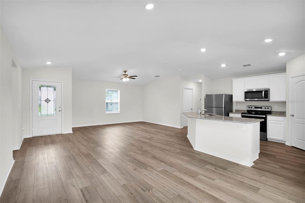 An open-concept kitchen and living area featuring white cabinets, stainless steel appliances, and wood-look flooring — 2 RYMSHAW PLACE, PALM COAST, FL