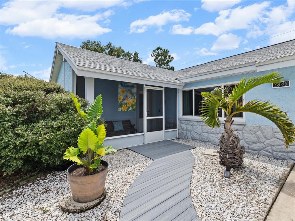 A blue house exterior features a screened front porch, a curved walkway, and landscaping — 3845 MING TREE DRIVE, NEW PORT RICHEY, FL