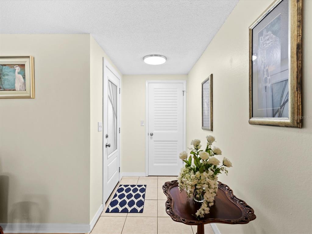 A tiled entryway features a white front door, a louvered closet door, and a floral arrangement — 3845 MING TREE DRIVE, NEW PORT RICHEY, FL