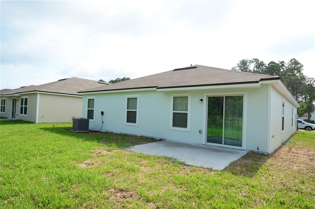 The exterior rear view of a light-colored house features a concrete patio and sliding doors — 664 GRAND RESERVE DRIVE, BUNNELL, FL