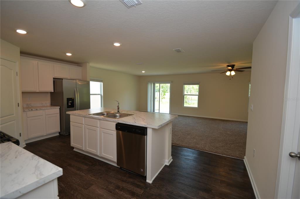 A kitchen with white cabinets and a marble-look island overlooks an open carpeted living area — 664 GRAND RESERVE DRIVE, BUNNELL, FL