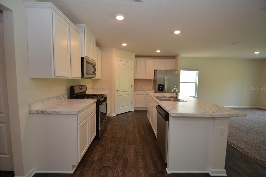 A kitchen features white cabinets, marble-look countertops, stainless steel appliances, and dark wood flooring — 664 GRAND RESERVE DRIVE, BUNNELL, FL
