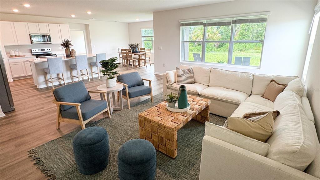 An open-concept living room features a white sectional sofa, two blue armchairs, and a kitchen — 17611 WHISKEY CREEK TRAIL, PARRISH, FL