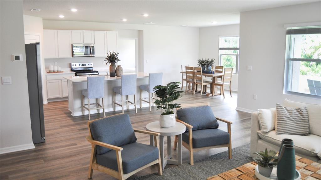 An open-concept kitchen, dining area, and living room feature white cabinets and wood-look flooring — 17611 WHISKEY CREEK TRAIL, PARRISH, FL