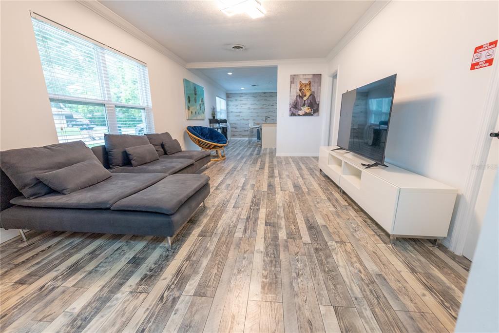 A living room features gray wood-look flooring, a large sectional sofa, and a wall-mounted television — 2627 AMBERGATE ROAD, WINTER PARK, FL