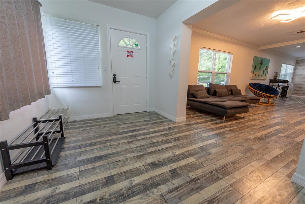 An entryway with wood-look tile flooring leads into a living room with a sectional sofa — 2627 AMBERGATE ROAD, WINTER PARK, FL