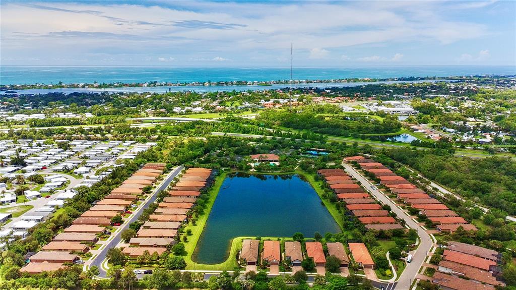 An aerial view shows a residential community with rows of houses surrounding a central lake — 5548 SENTIERO DRIVE, NOKOMIS, FL