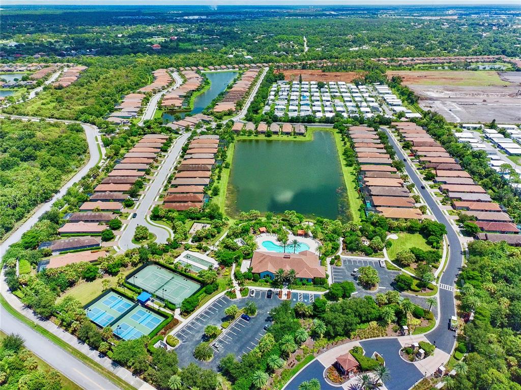 Aerial view of a residential community featuring a central lake, clubhouse, pool, and tennis courts — 5548 SENTIERO DRIVE, NOKOMIS, FL