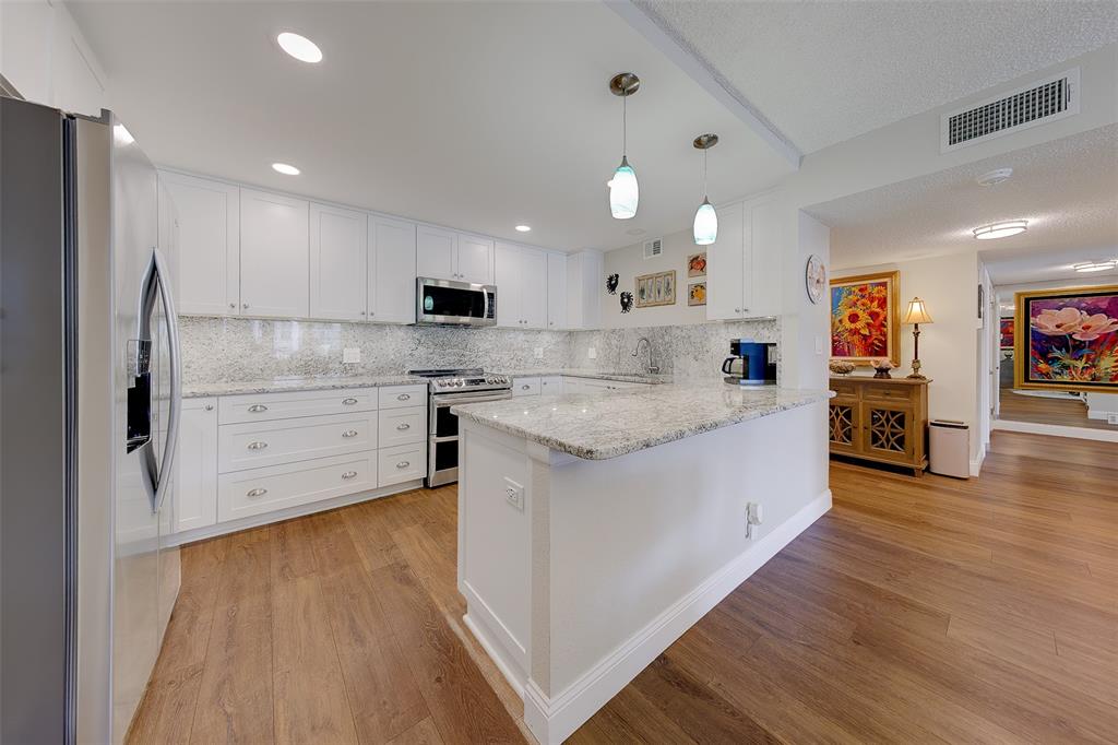 A modern kitchen features white cabinetry, granite countertops, and wood-look flooring — 1460 GULF BOULEVARD UNIT 305, CLEARWATER, FL