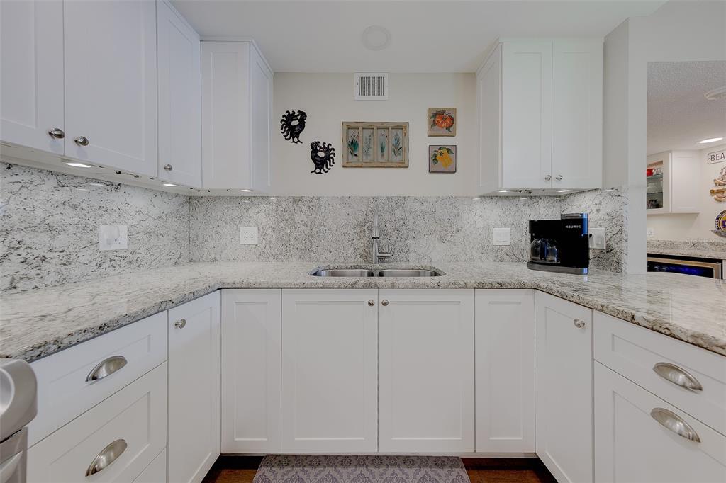 A kitchen features white cabinets, granite countertops, a double sink, and decorative wall art — 1460 GULF BOULEVARD UNIT 305, CLEARWATER, FL