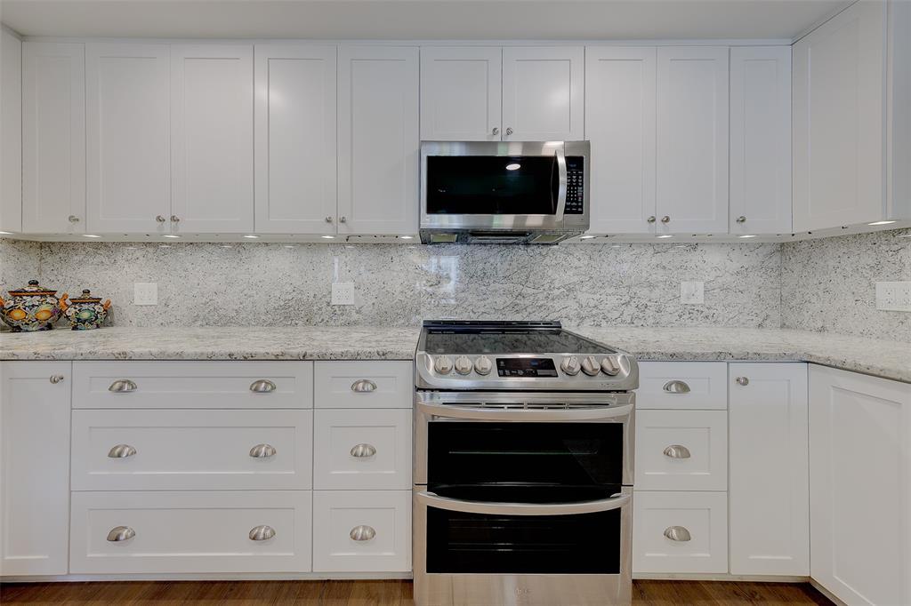 A kitchen features white shaker cabinets, stainless steel appliances, and a speckled granite countertop — 1460 GULF BOULEVARD UNIT 305, CLEARWATER, FL