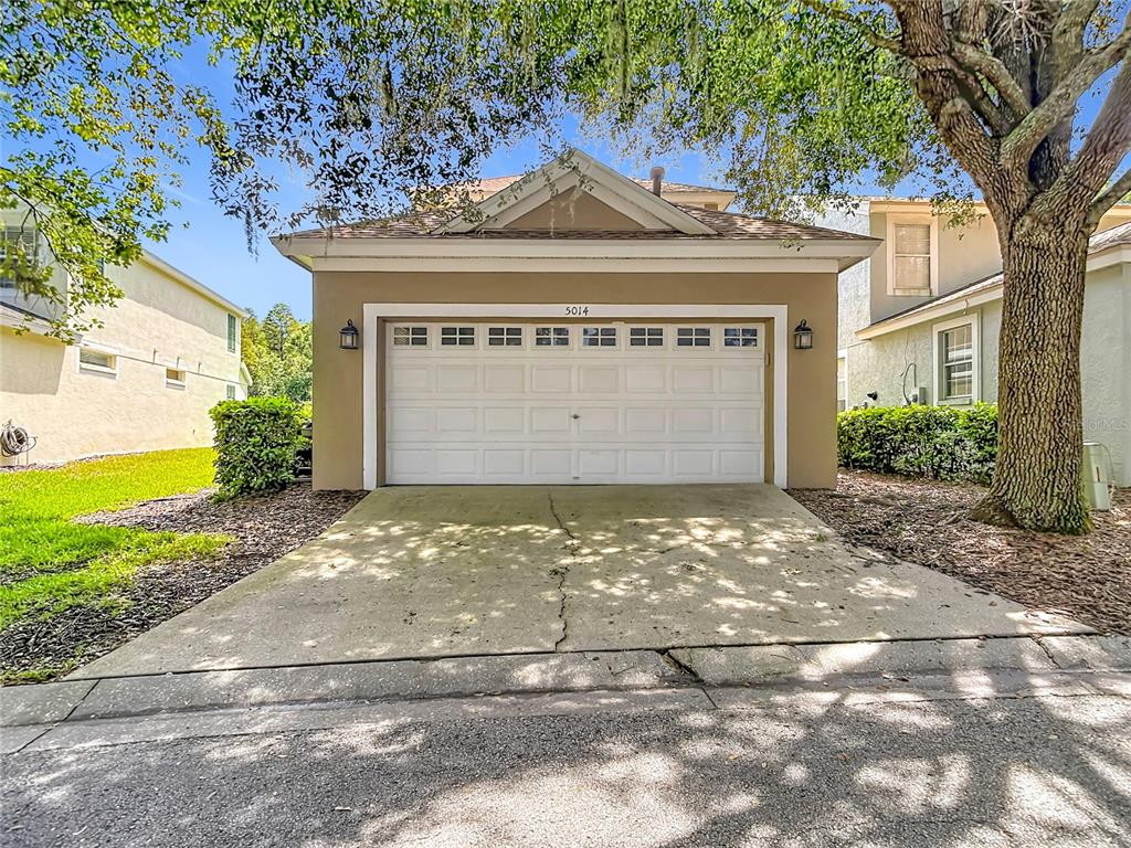 A detached garage with a white sectional door and a concrete driveway under a tree — 5014 BRIDGEWAY LANE, LUTZ, FL